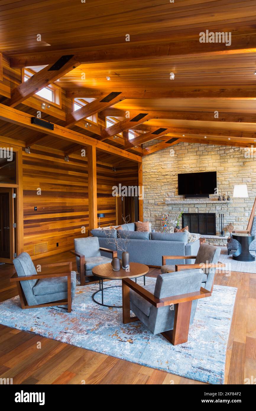 Fauteuils rembourrés en bois brun et gris, table ronde et canapés avec cheminée en pierre naturelle dans la salle de séjour à l'intérieur d'une maison en bois de cèdre. Banque D'Images