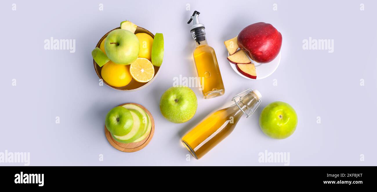 Composition avec bouteilles de vinaigre de cidre de pomme et fruits frais sur fond clair, vue du dessus Banque D'Images