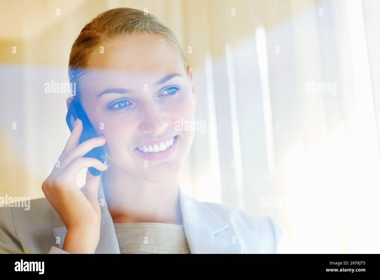 Femme d'affaires souriante ayant une conversation sur un téléphone portable. Jolie jeune femme d'affaires parlant au-dessus du téléphone portable, vue à travers un verre. Banque D'Images