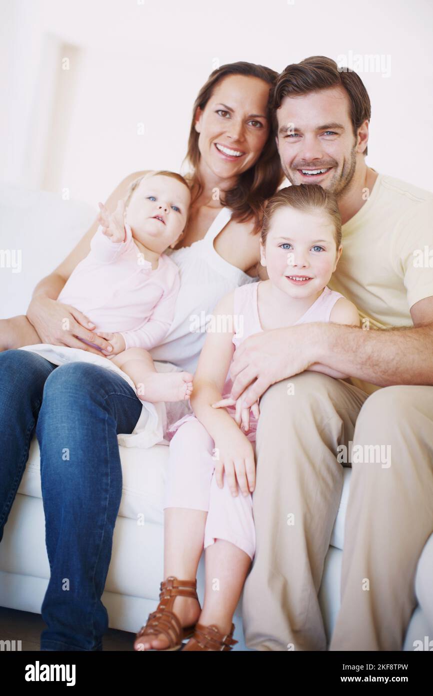 Rencontrez la famille heureuse de quatre personnes. Portrait en gros plan d'une famille avec deux enfants assis ensemble sur un canapé à l'intérieur. Banque D'Images