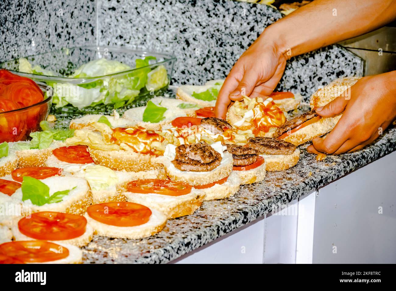 Assiette de laitue et de tomates sur le plan de travail, sur les hamburgers ouverts en rangée avec des frites, des steaks grillés hachés et de la sauce ketchup. Banque D'Images