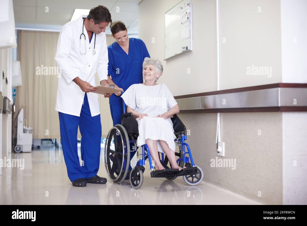 Ce n'est rien de grave. Une infirmière qui pousse une patiente en fauteuil roulant dans le passage pendant qu'elle parle avec son médecin. Banque D'Images