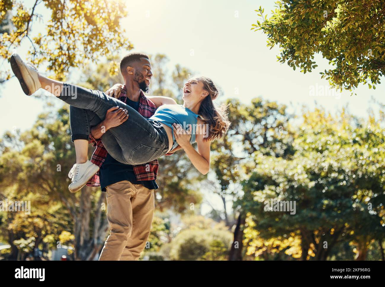 Jeune couple interracial, parc et homme portant la femme à la date d'été dans le jardin, plaisir de soleil ou de se détendre, amour et soin ensemble. Couple heureux, sourire et Banque D'Images