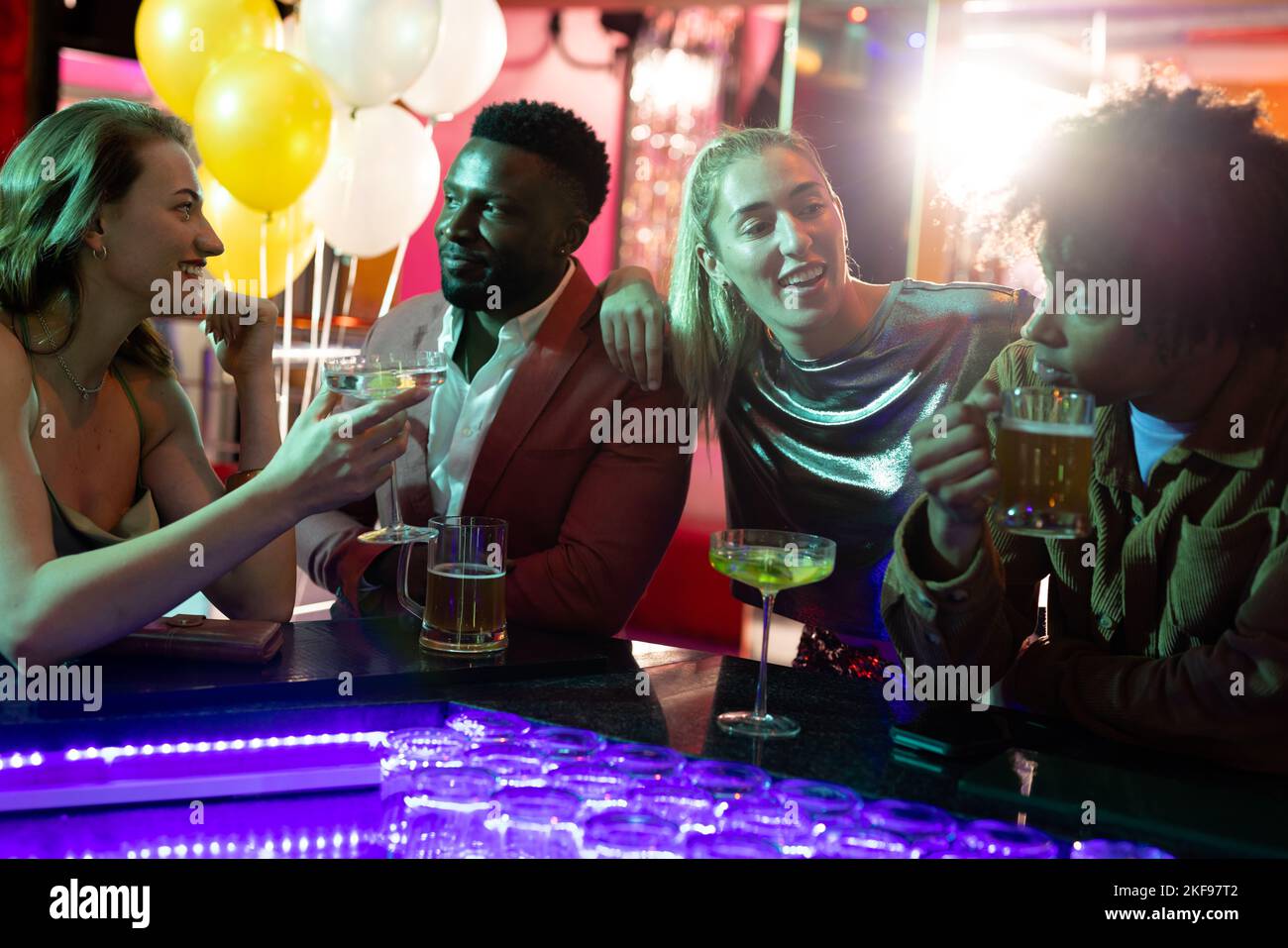 Un groupe heureux d'amis hommes et femmes qui boivent et parlent au bar dans une boîte de nuit Banque D'Images