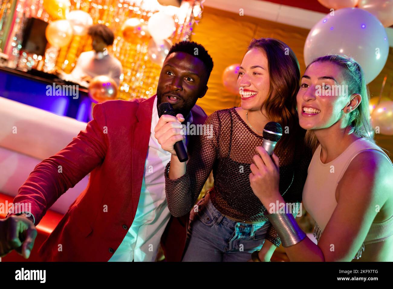 Trois amis masculins et féminins différents qui chantent du karaoké dans un bar de discothèque Banque D'Images