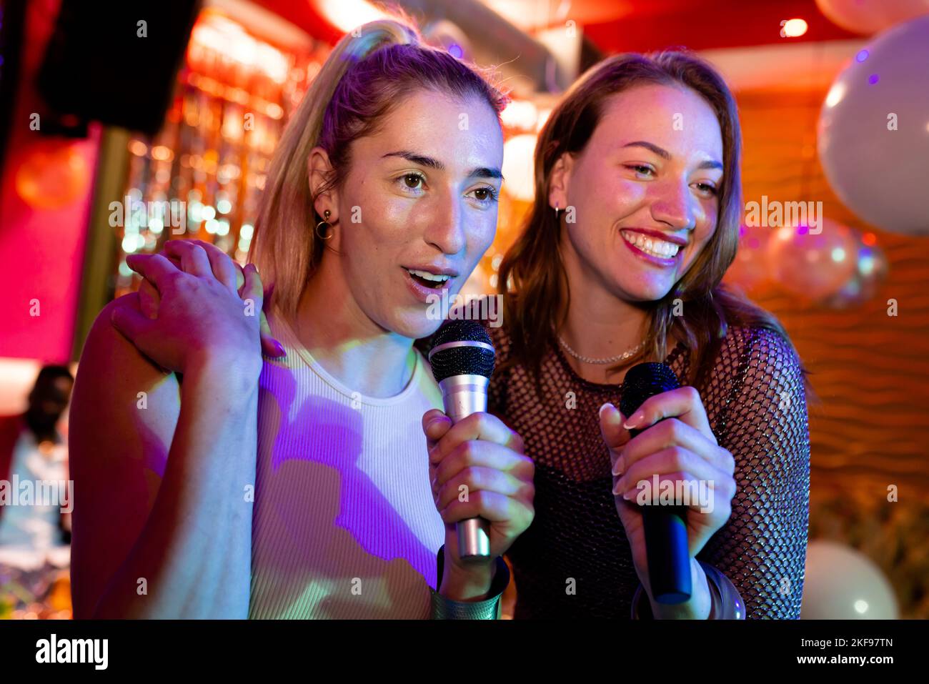 Deux amies caucasiennes qui chantent du karaoké au bar de la discothèque Banque D'Images