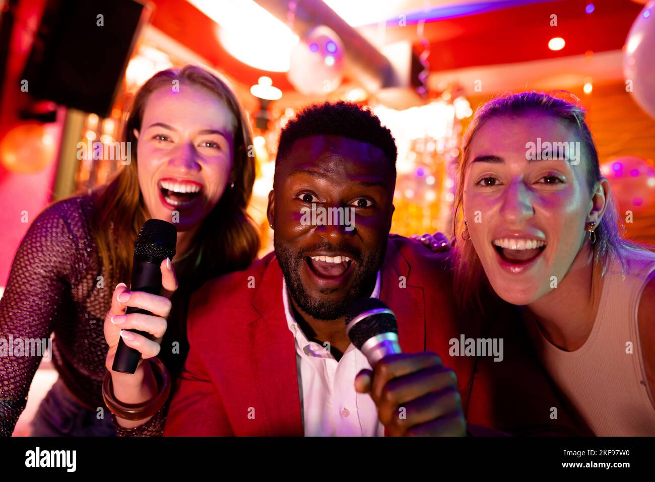 Portrait de trois amis hommes et femmes heureux et variés chantant du karaoké au bar de la discothèque Banque D'Images