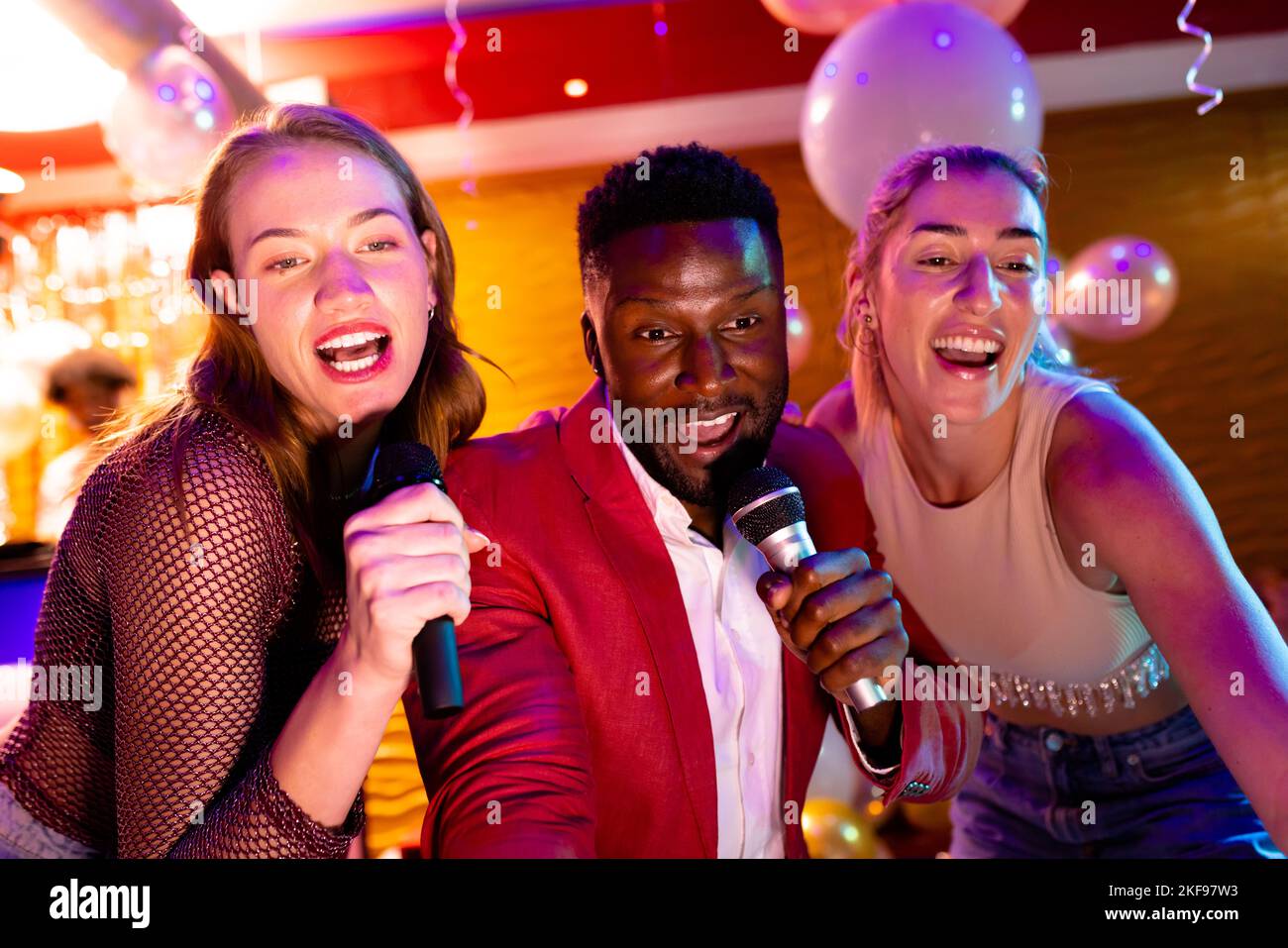 Trois amis masculins et féminins différents qui chantent du karaoké dans un bar de discothèque Banque D'Images