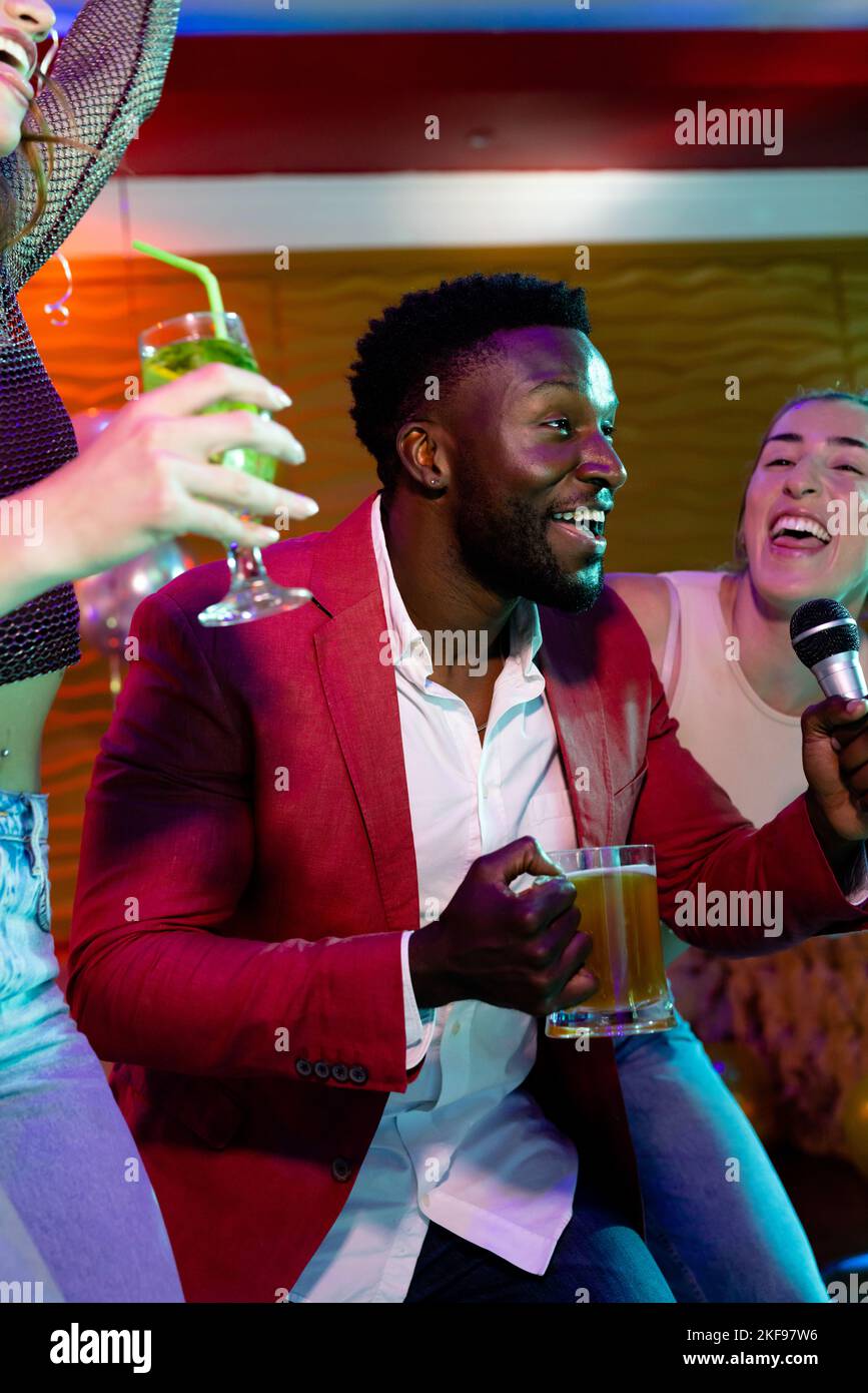 Vertical de l'homme afro-américain heureux et de diverses amies chantant karaoké au bar de boîte de nuit Banque D'Images