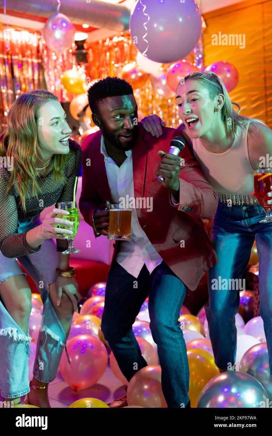Verticale de trois amis hommes et femmes heureux et variés chantant du karaoké, buvant au bar de la discothèque Banque D'Images