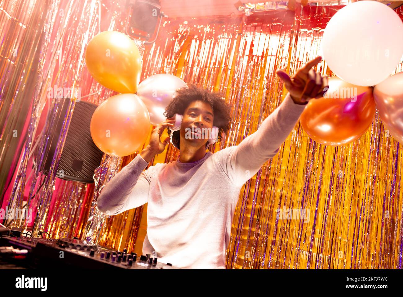 DJ afro-américain souriant dans des écouteurs jouant de la musique dans une boîte de nuit et pointant Banque D'Images