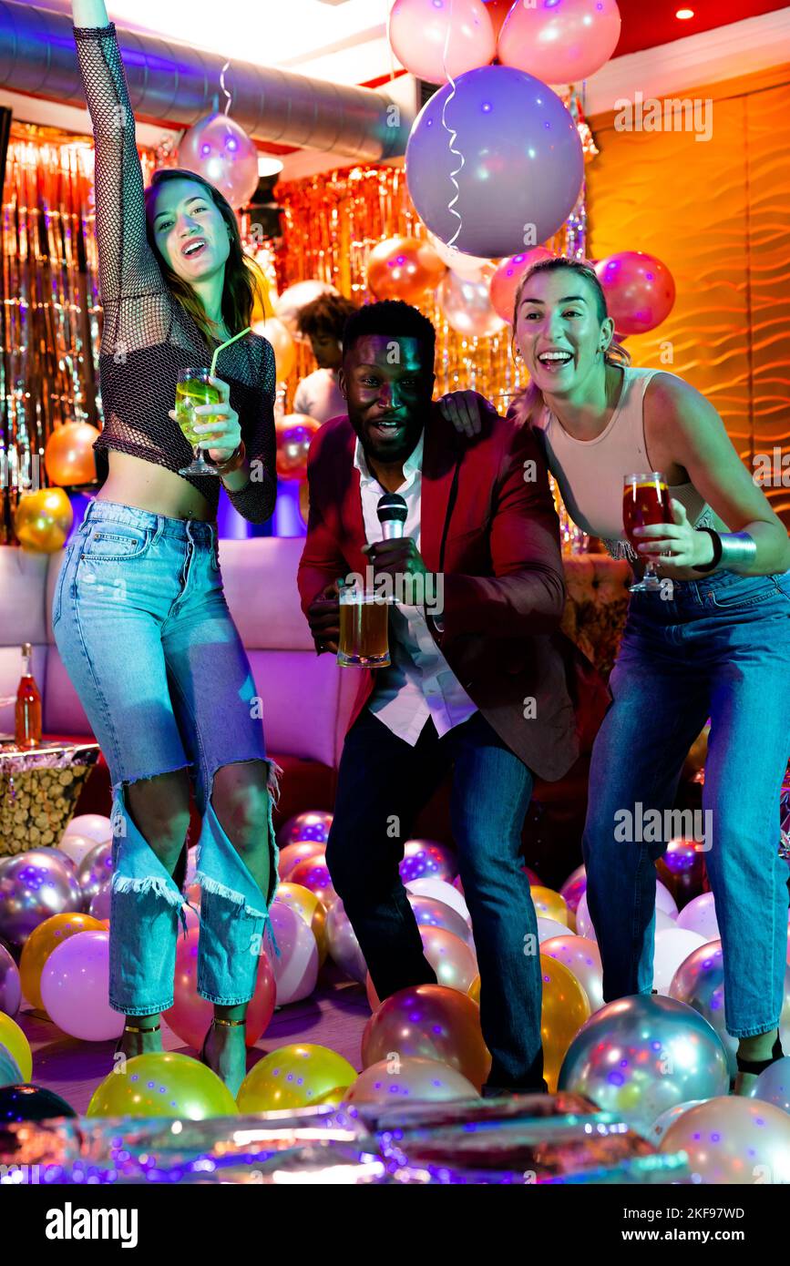 Verticale de trois amis hommes et femmes heureux et variés chantant du karaoké, buvant au bar de la discothèque Banque D'Images