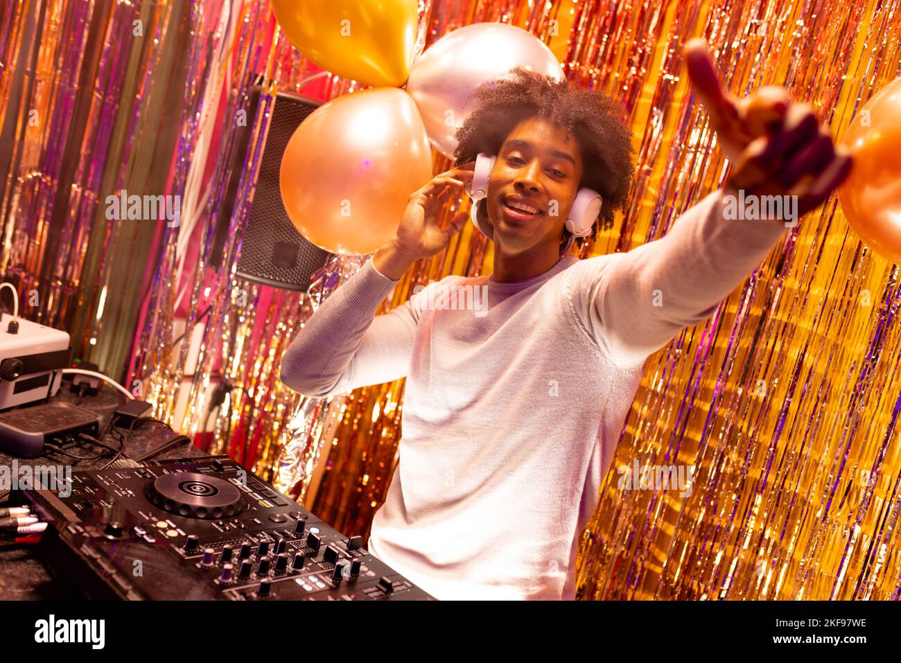 DJ afro-américain souriant dans des écouteurs jouant de la musique dans une boîte de nuit et pointant Banque D'Images