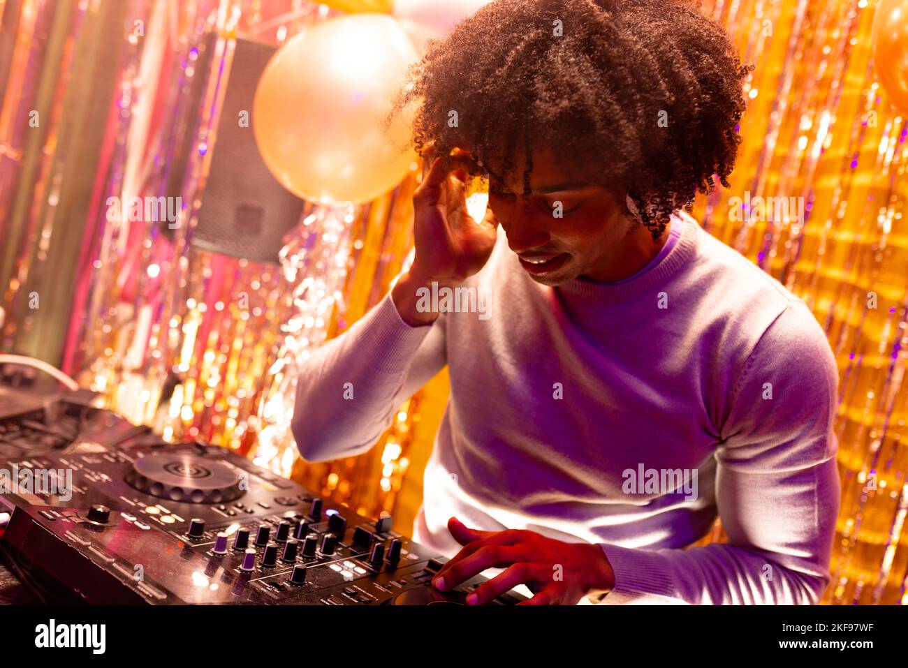 Un DJ afro-américain souriant joue de la musique dans une boîte de nuit et mélange Banque D'Images