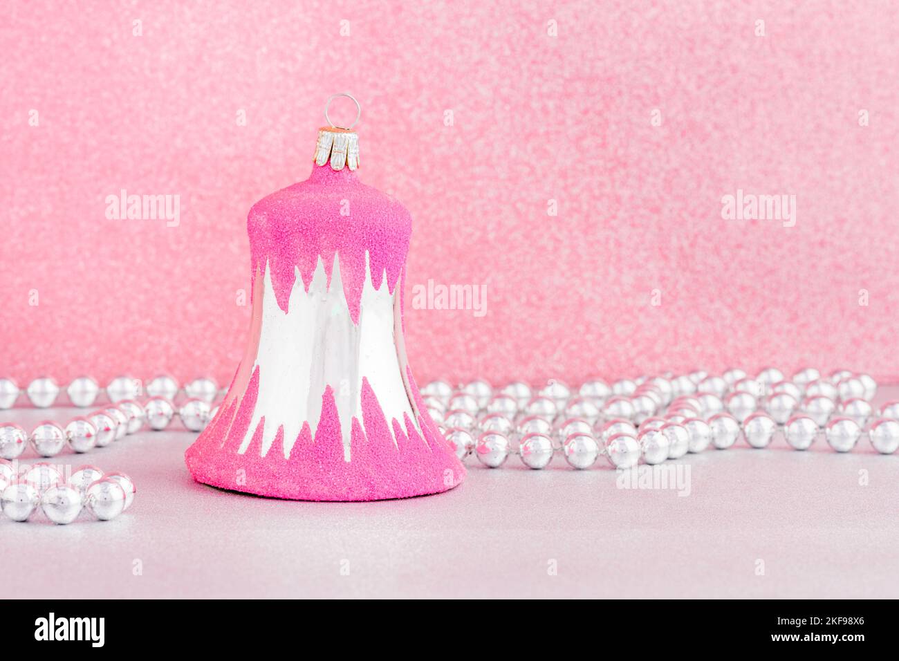 Une boule de noël rose vintage en forme de cloche avec une guirlande argentée ornée de perles sur fond rose. Banque D'Images