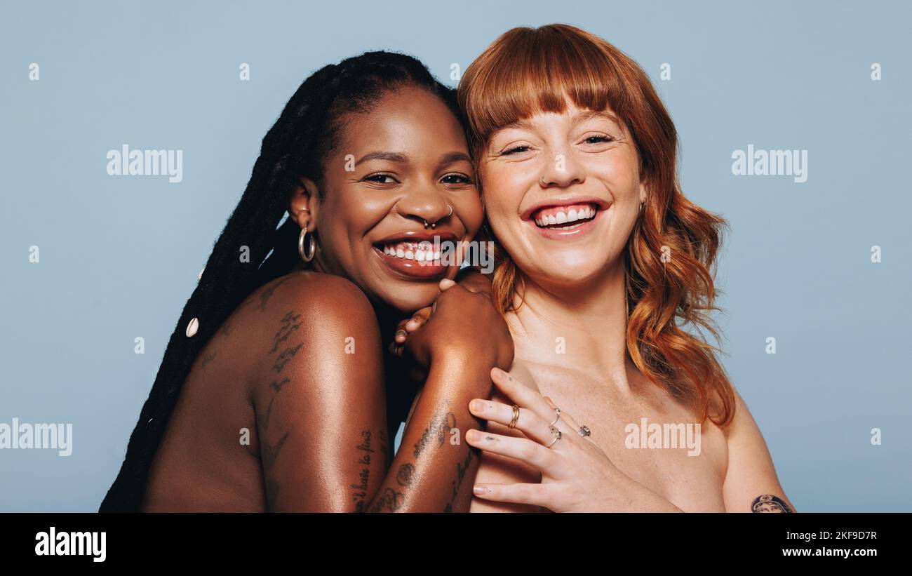 Des femmes heureuses avec différentes tons de peau souriant à l'appareil photo tout en se tenant debout ensemble. Deux jeunes femmes en confiance dans le corps embrassent leur beauté naturelle. CH Banque D'Images