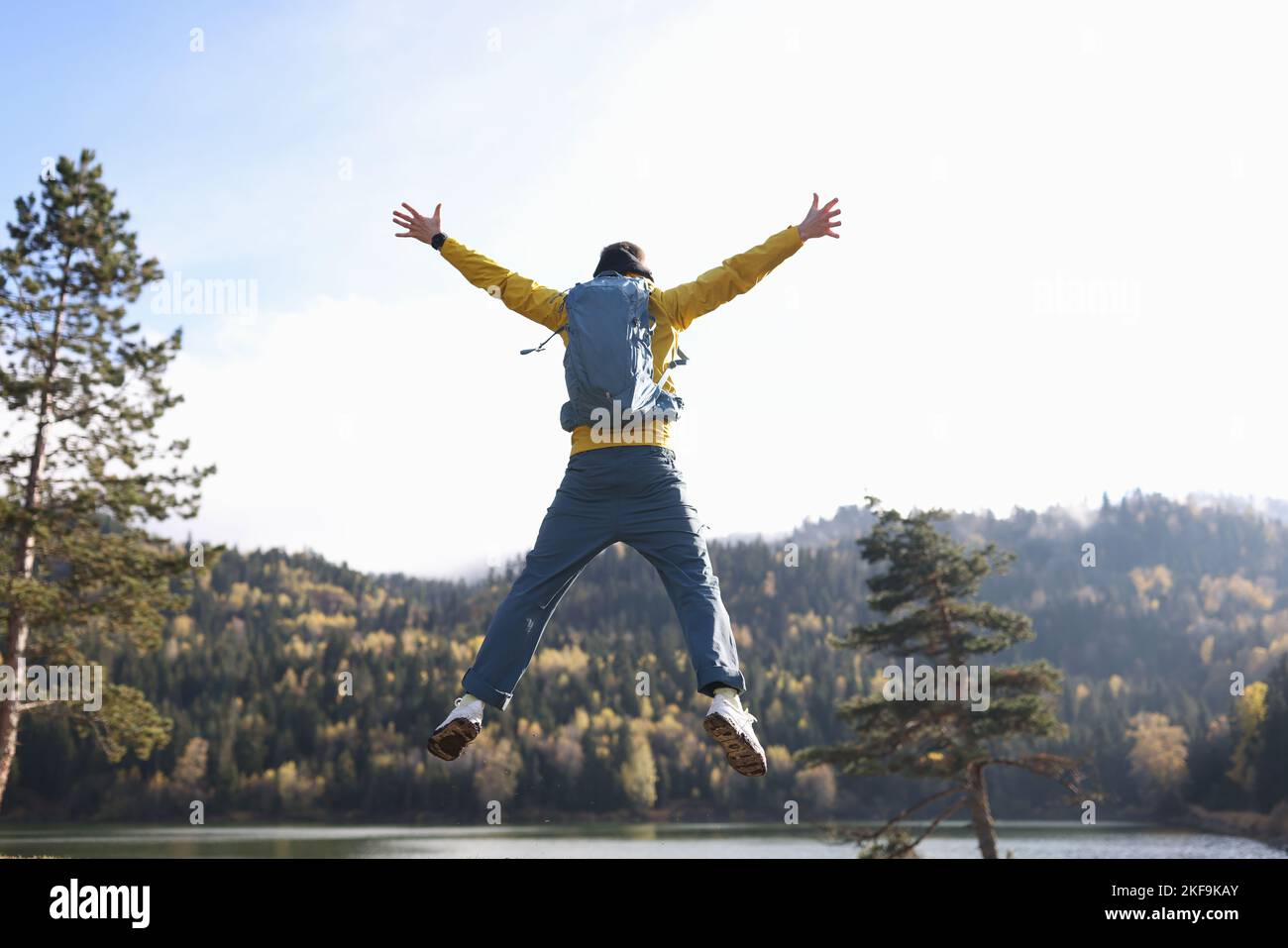 Homme heureux avec saut à bras ouverts, lac et montagnes en arrière-plan. Banque D'Images