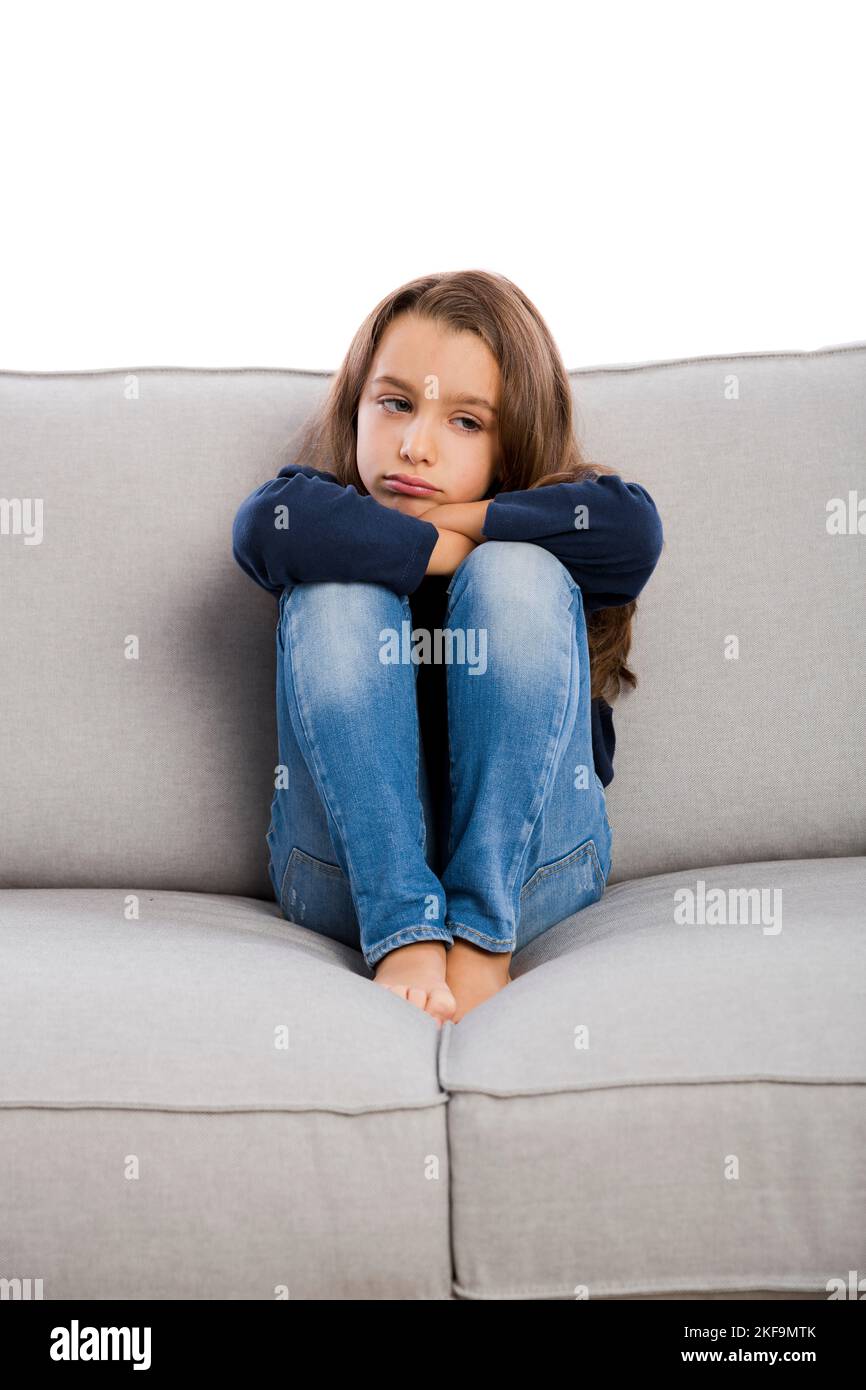 Petite fille assise sur un canapé et bouleversée avec un visage ennuyé Banque D'Images