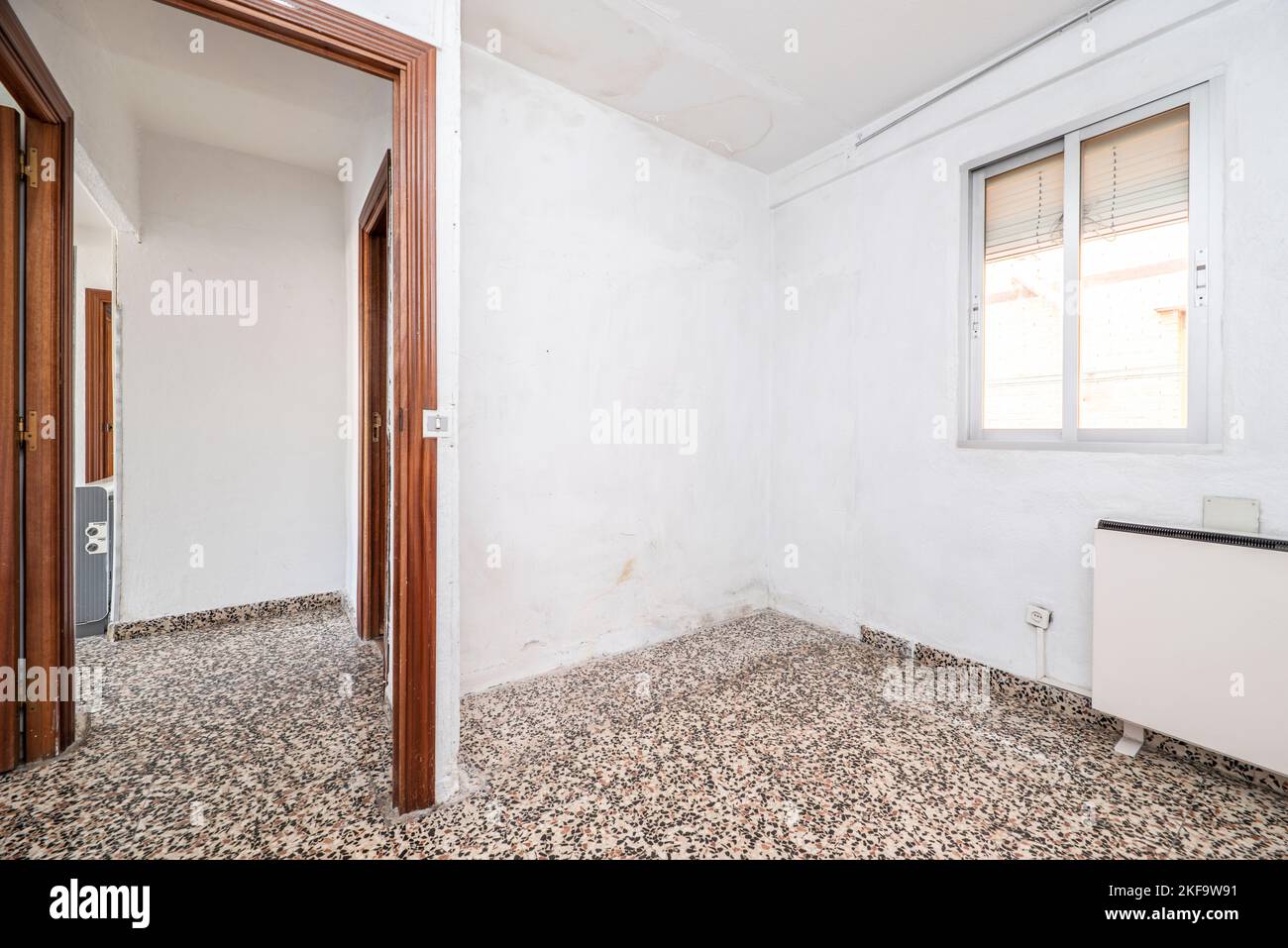 Salon vide avec sol en terrazzo gris brillant avec murs peints en blanc, menuiserie de porte rougeâtre et fenêtre avec volets roulants Banque D'Images