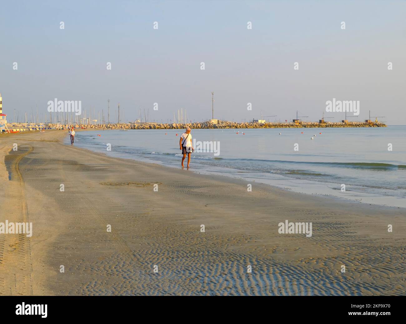 Juillet 2022 Senigallia, Italie: Homme aîné marchant vers la caméra sur la plage à travers la mer, le ciel de lever du soleil, et l'horizon Banque D'Images