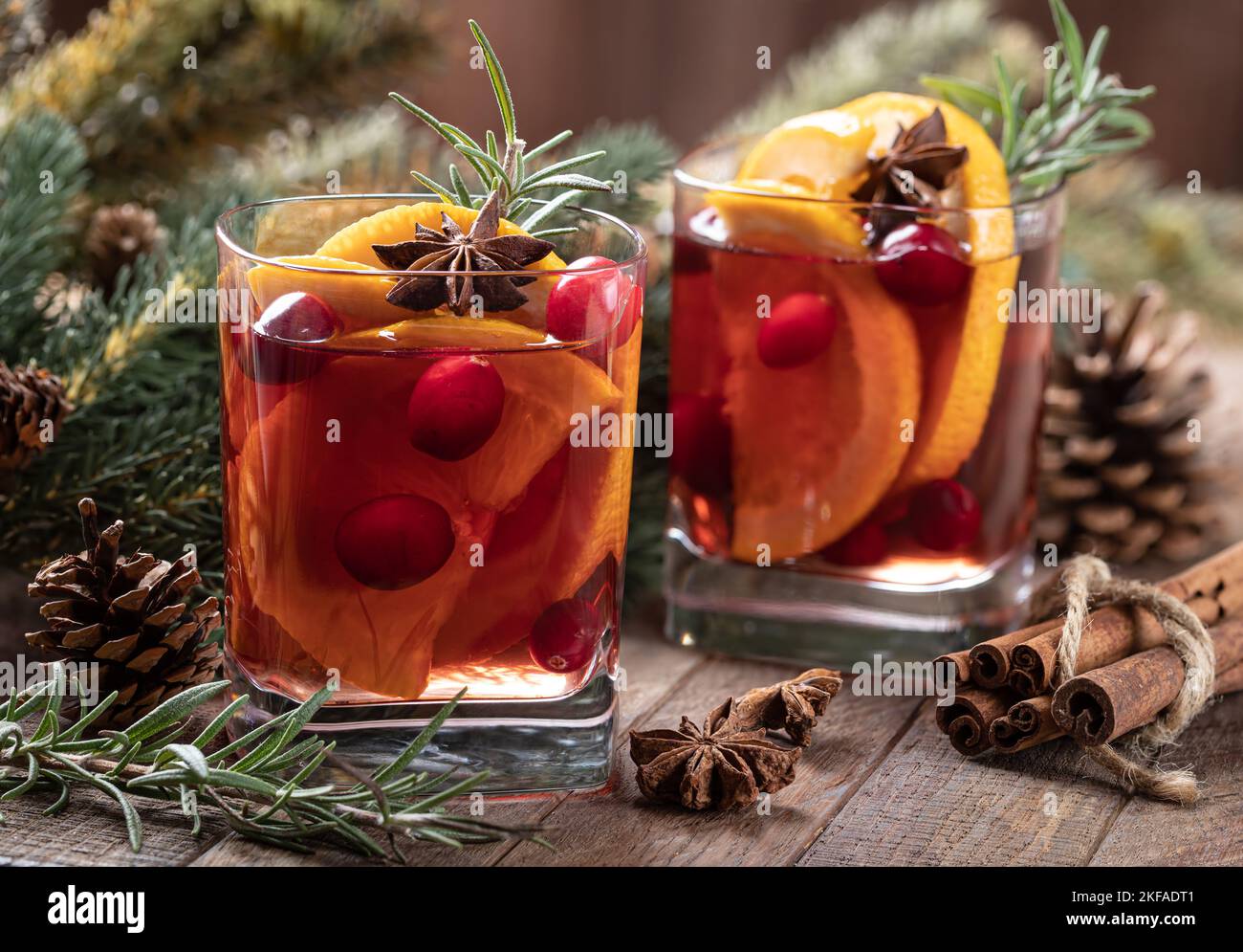 Vin chaud accompagné de tranches d'orange, de canneberges et d'épices sur une table en bois rustique avec décoration d'arbre de Noël en arrière-plan Banque D'Images