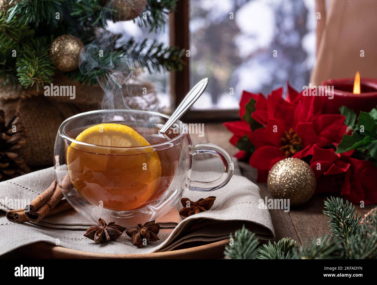 Thé chaud à la vapeur avec une tranche de citron et des décorations de vacances par une fenêtre avec fond d'hiver Banque D'Images