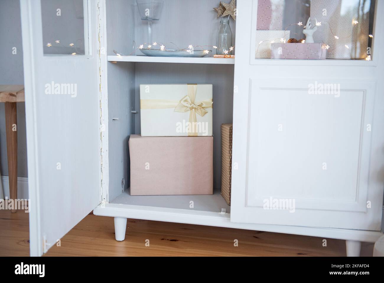 Il y a des boîtes de vacances roses attachées avec un ruban d'or dans un panneau latéral en bois blanc. Une guirlande lumineuse crée une atmosphère festive dans la maison. Christma Banque D'Images