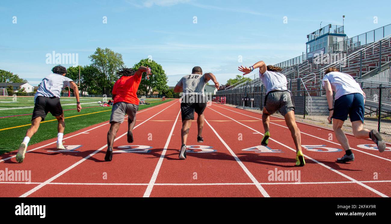 Vue arrière de cinq garçons d'école secondaire qui font un sprint rapide à l'entraînement dans les voies sur une piste. Banque D'Images