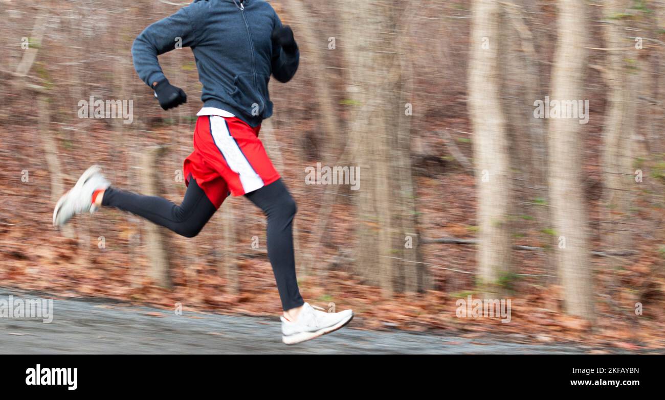 Arrière-plan et jambes flous d'un coureur d'école secondaire court rapidement dans les bois pendant la pratique de la piste. Banque D'Images