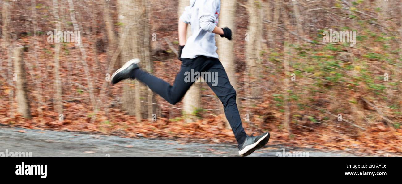 Un coureur de lycée qui court rapidement dans les bois avec un arrière-plan flou et des jambes floues. Banque D'Images