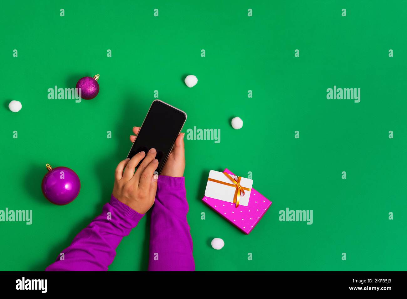 Mains dans un chandail violet touche l'écran du smartphone avec les doigts, paiement en ligne pour les achats de Noël, fond vert, plat. Conflue lumineuse Banque D'Images