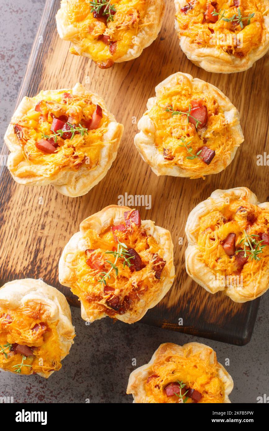 Des muffins rustiques à la pâte feuilletée farcis avec des œufs, du fromage et du jambon sur une planche en bois sur la table. Vue verticale du dessus Banque D'Images