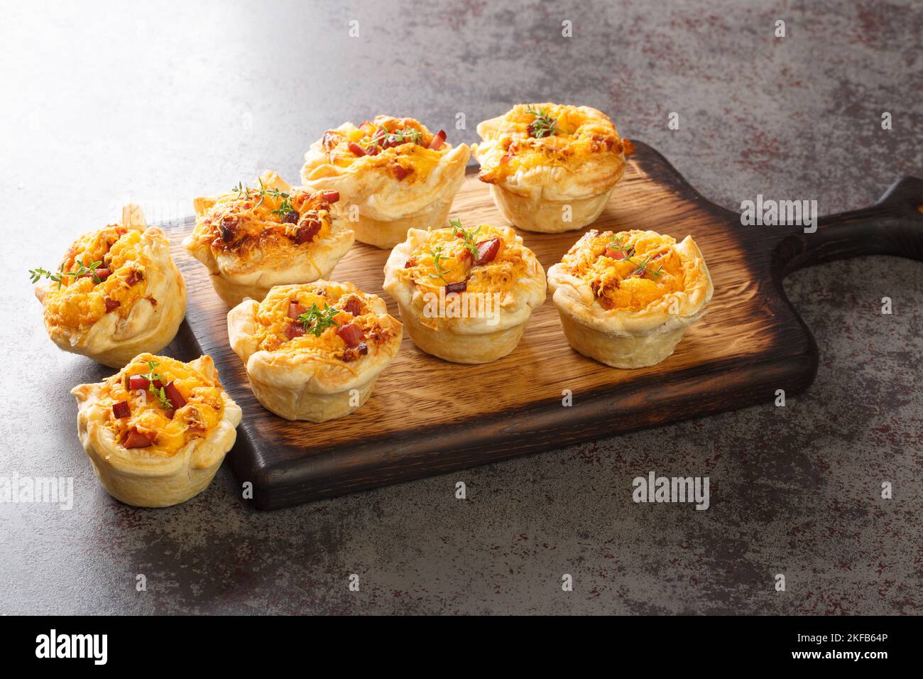 Mini-tasses croustillantes de pâte feuilletée farcies aux œufs, au fromage et au jambon sur une planche de bois sur la table. Horizontale Banque D'Images