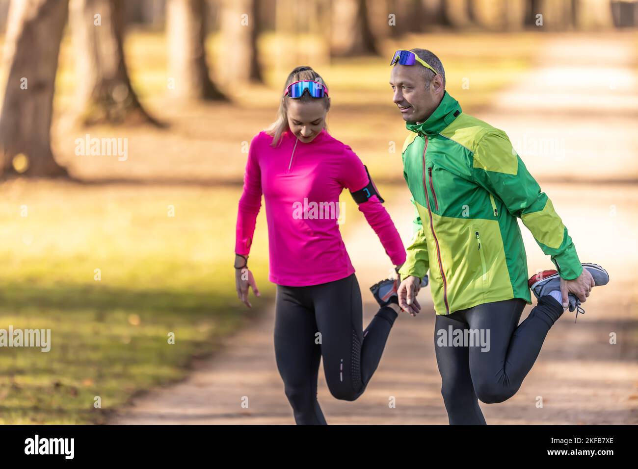 Deux athlètes amateurs mature homme et jeune femme se réchauffent avant de courir, faisant le corps inférieur s'étirant dans le parc. Banque D'Images
