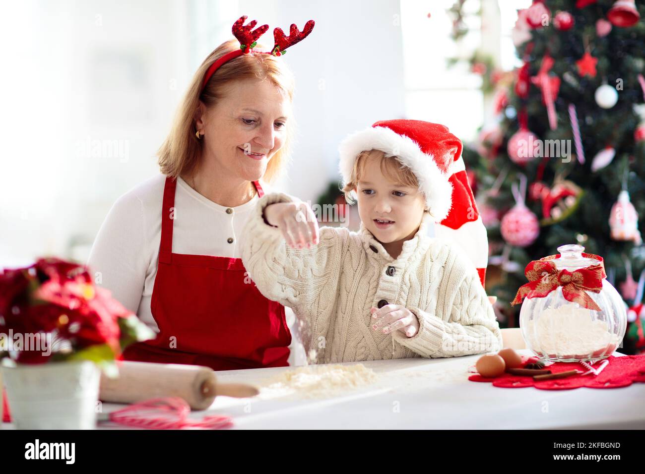 Petits gâteaux de Noël pour toute la famille.Grand-mère et enfant font  cuire la pâte de pain d'épice.Fêtes de Noël pour les enfants.Petit garçon  en chapeau de père Noël faisant de la pâte