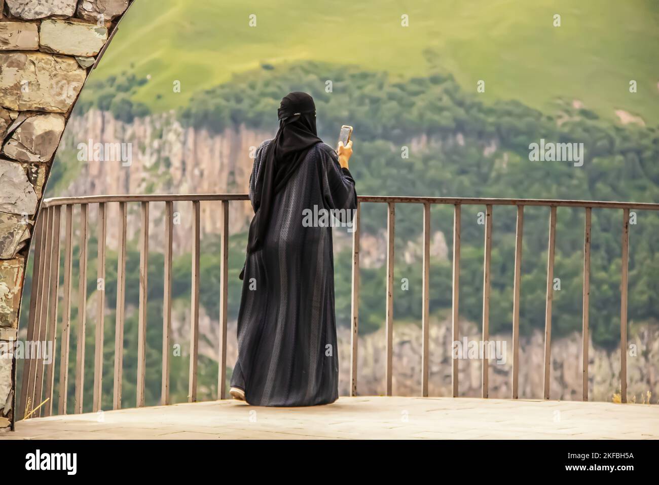 Vue d'une femme à niqab ou burqa debout sur le rail en prenant une photo de la vue panoramique avec un téléphone cellulaire Banque D'Images