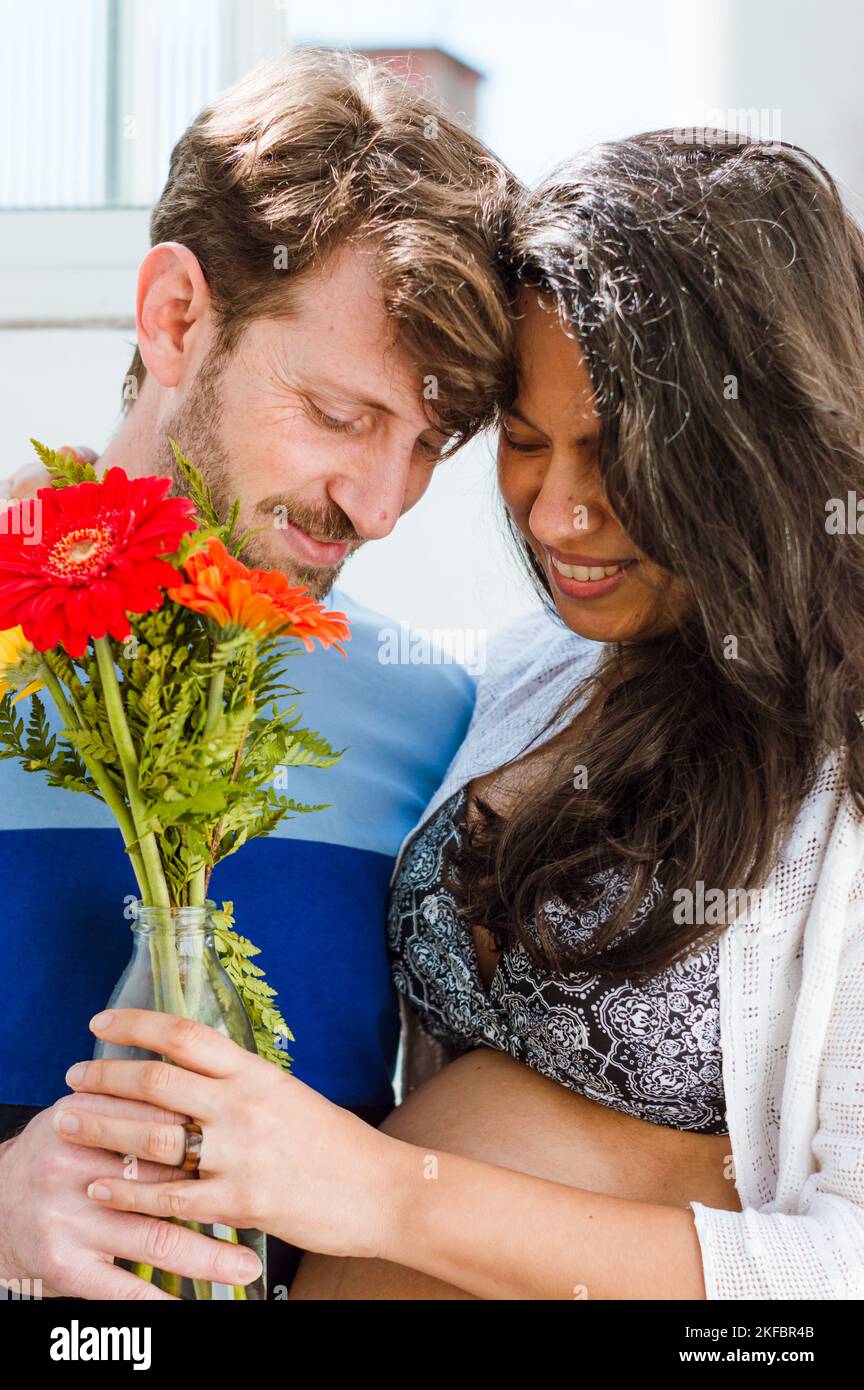 portrait d'un couple hétérosexuel latino enceinte, amoureux d'un bouquet de fleurs et regardant vers le bas et avec leurs têtes sur le front Banque D'Images