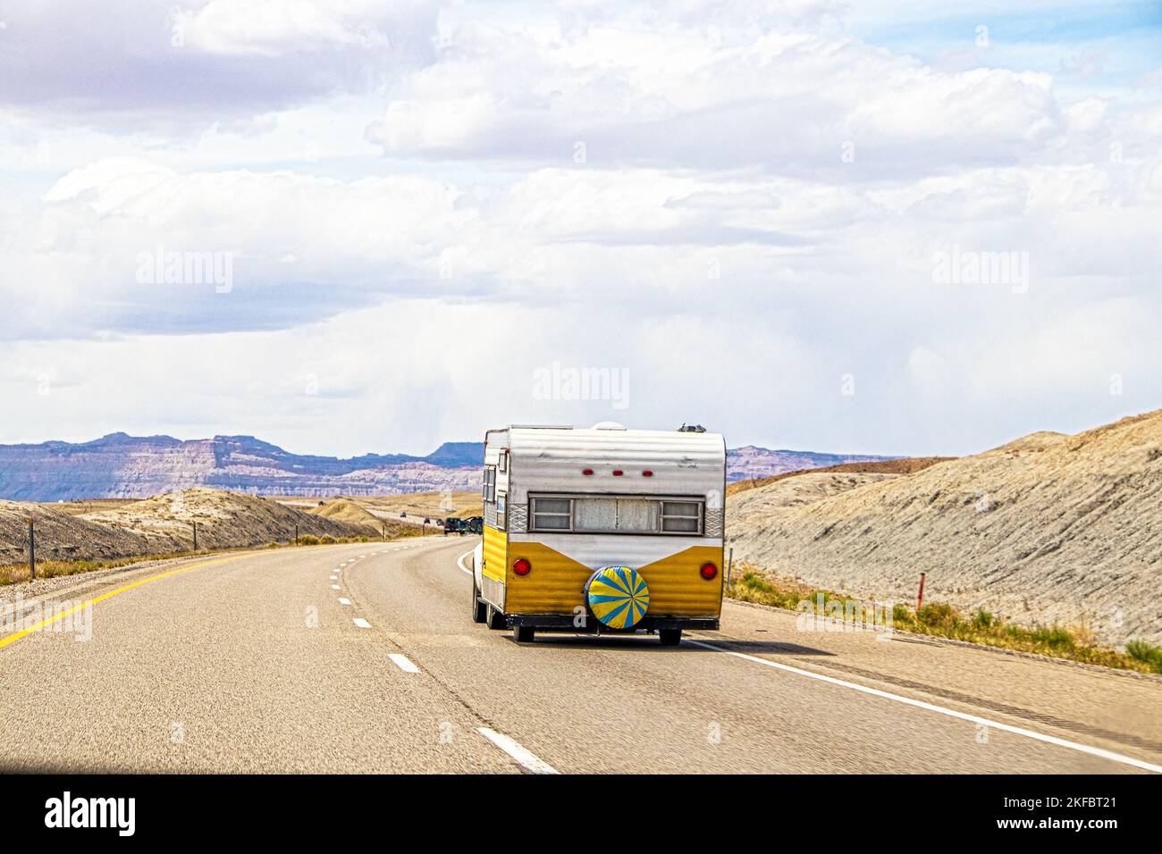 Une fourgonnette rétro jaune et blanche part en voiture dans la région des badlands de l'Utah, près du parc national d'Arches, avec départ dessert sur une route à deux voies Banque D'Images