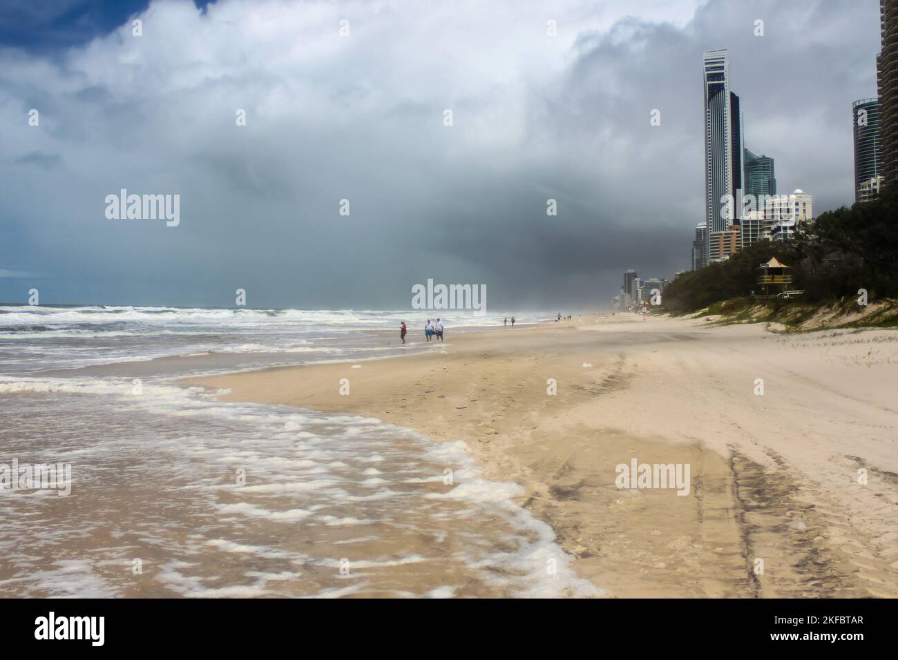 Des pistes de pneus et des touristes non identifiables sur la plage se frayant un chemin dans le surf le jour de la tempête avec des nuages sombres à Gold Coast - Surfers Paradise Australia avec c Banque D'Images