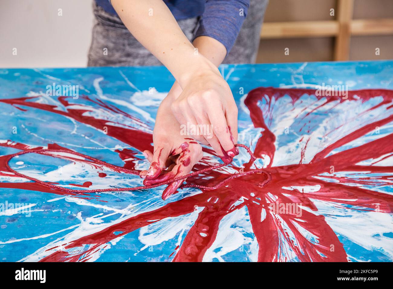 Gros plan des mains croisées d'une femme artiste colorée avec peinture avec corde photo abstraite de fleur sur toile. Banque D'Images