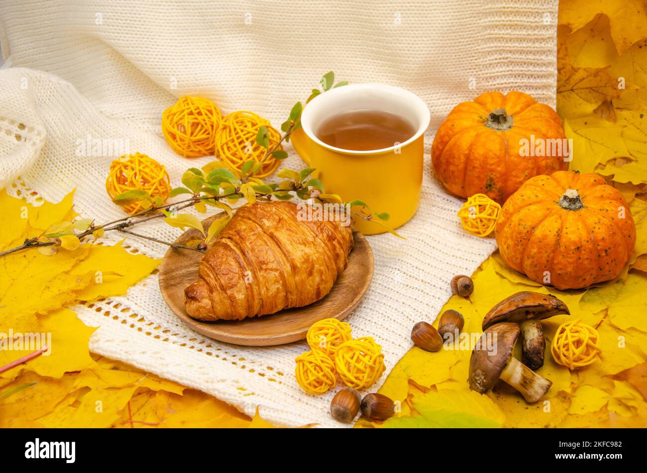 L'automne encore vie dans les tons jaune-orange: Un tricoté blanc à carreaux et feuilles, une tasse jaune et un croissant Banque D'Images