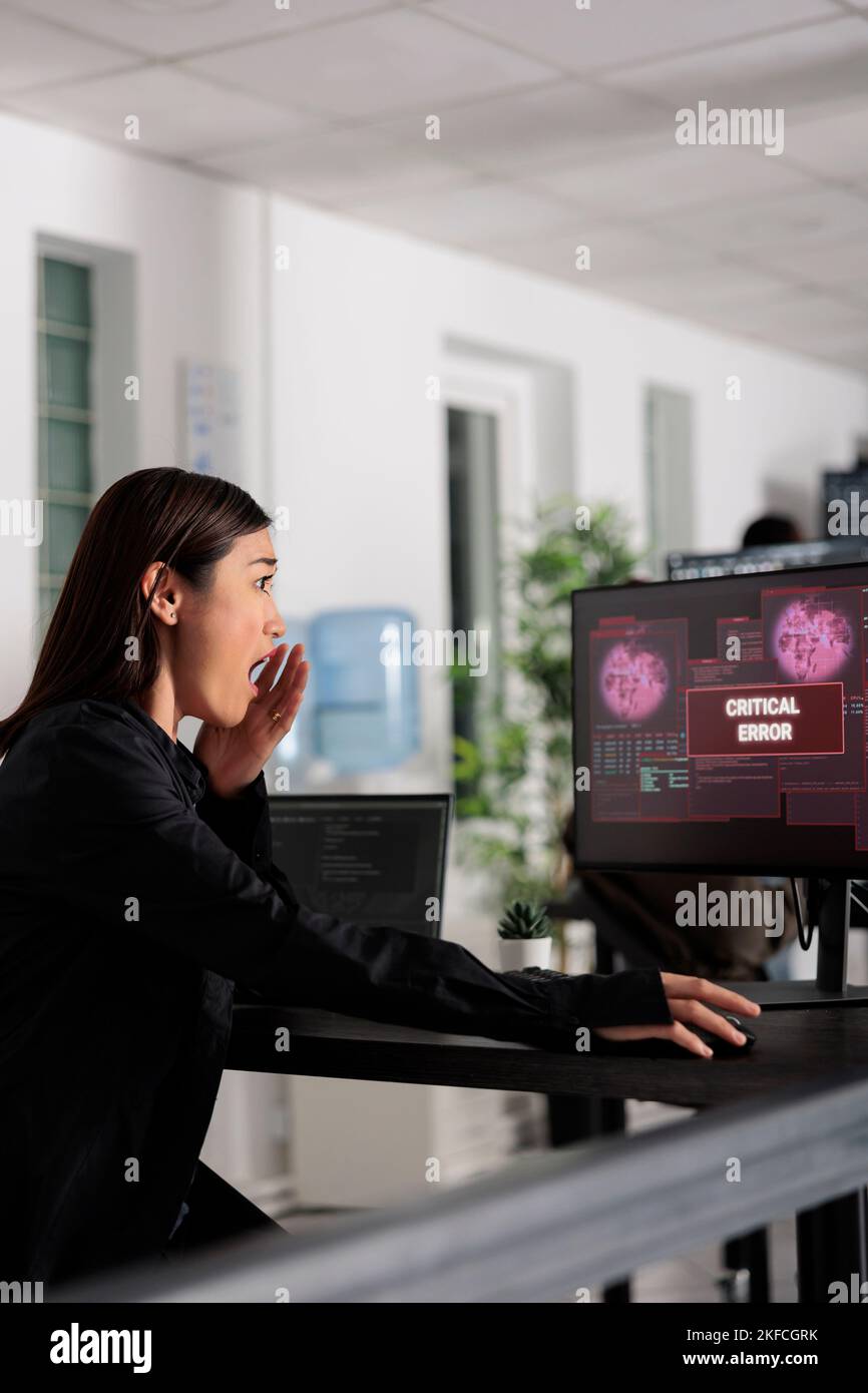 Développeur de logiciels femme ayant un serveur Web piraté, regardant l'erreur critique sur l'écran d'ordinateur dans le bureau. Programmeur asiatique essayant de résoudre le problème de piratage, sécurité de pare-feu. Banque D'Images