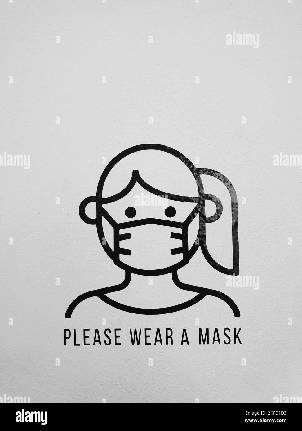 Veuillez porter un autocollant de masque avec l'illustration minimaliste d'une fille couvrant la bouche et le nez avec un. Sécurité COVID-19 rappel pandémique sur un mur blanc. Banque D'Images