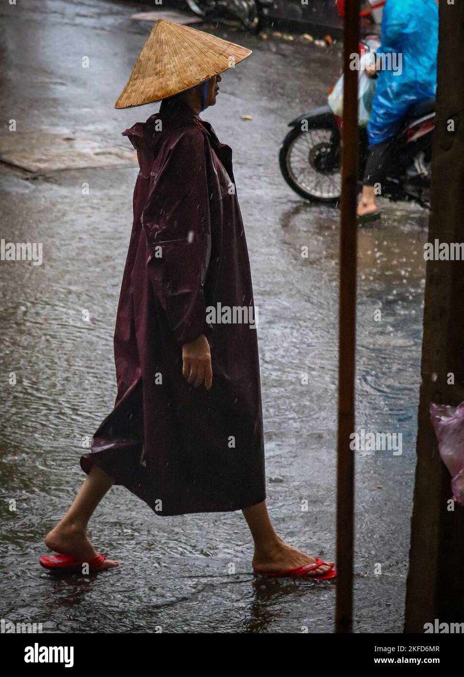 Photo verticale d'une femme en flip flops et imperméable portant un chapeau conique asiatique traditionnel à l'extérieur Banque D'Images
