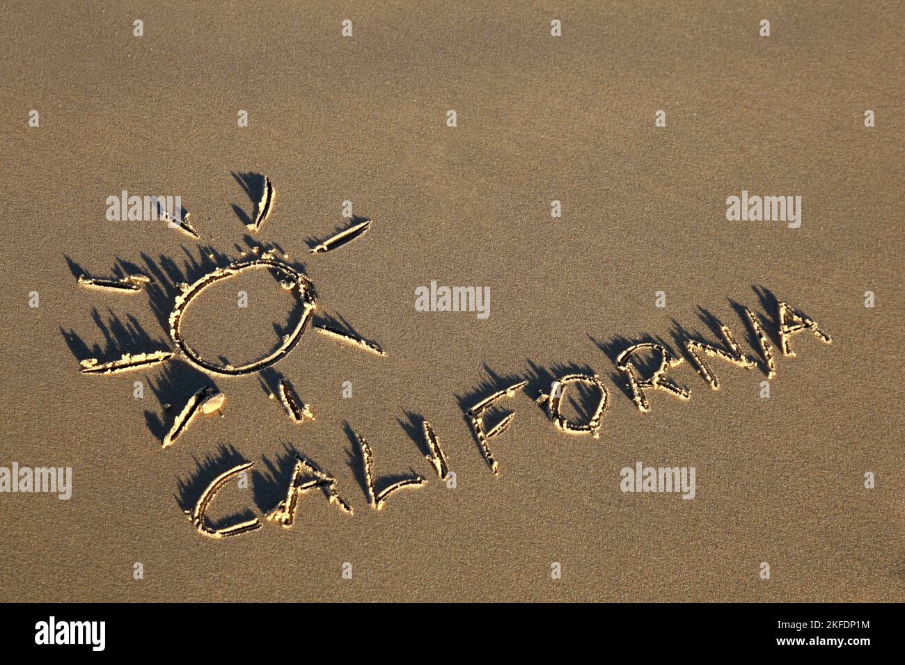 La Californie a écrit dans le sable à la plage avec le symbole du soleil. Banque D'Images