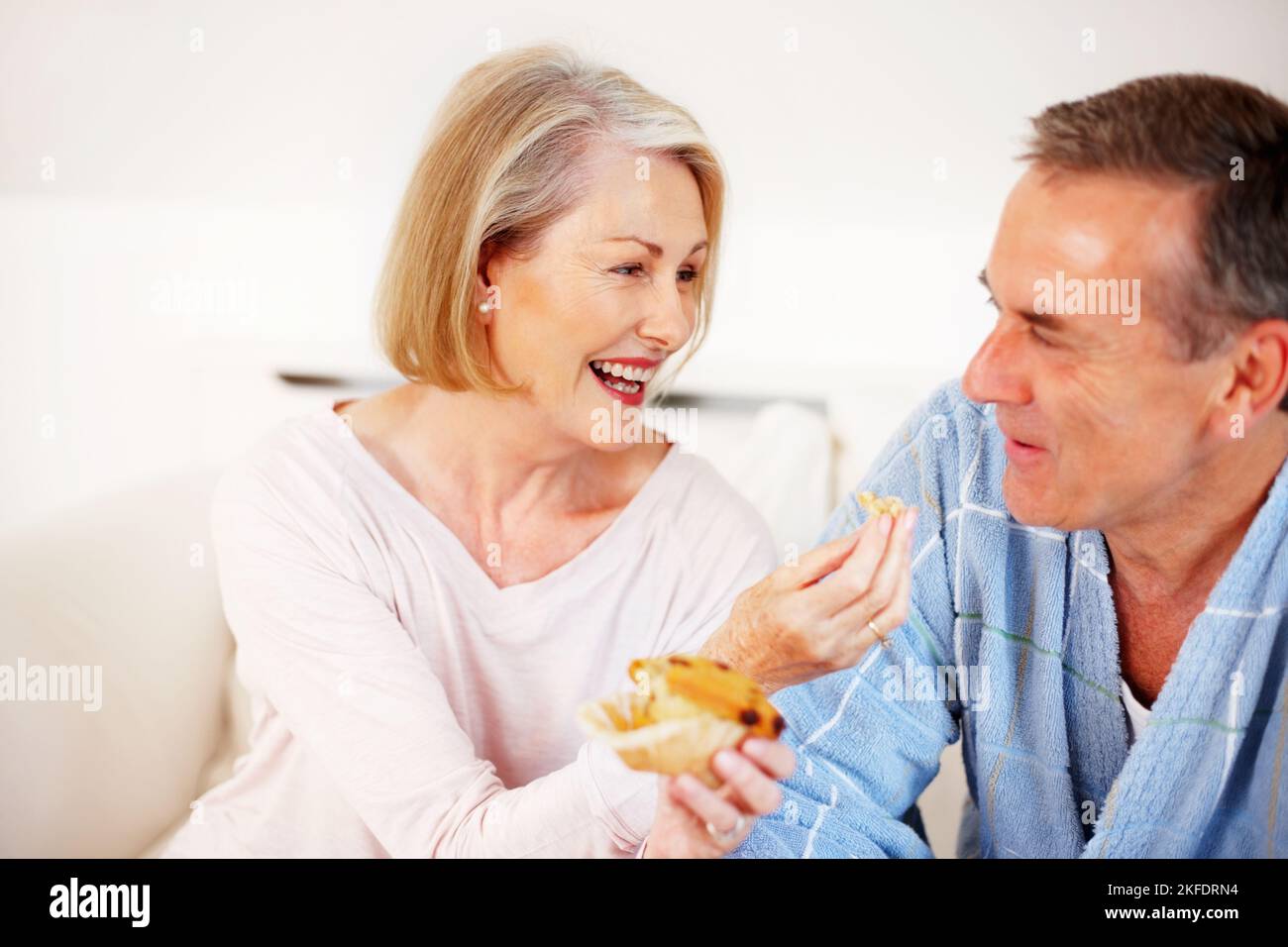 Bonne humeur femme mûre nourrissant un muffin à son mari. Portrait d'une femme mûre et gaie qui nourrit son mari de muffin. Banque D'Images