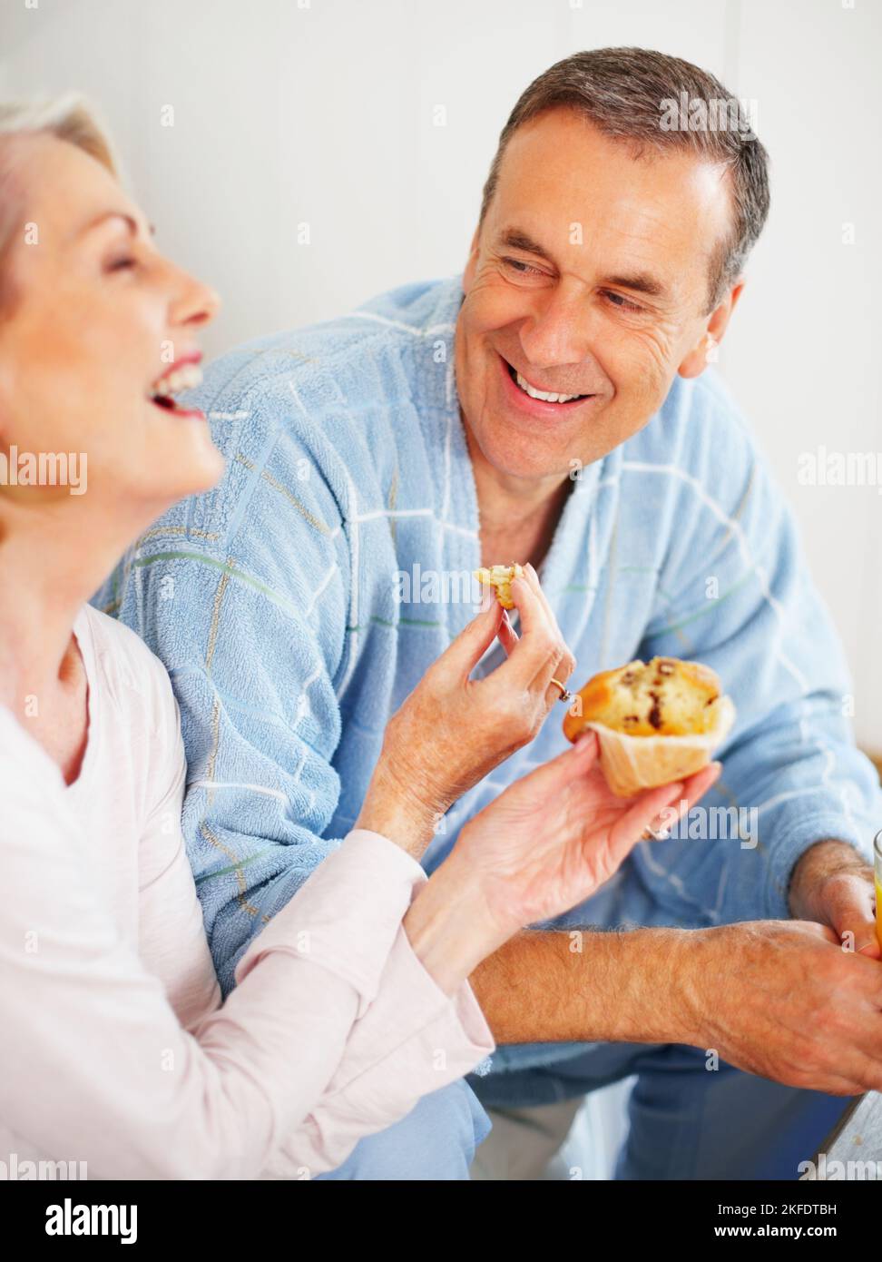 Bonne humeur femme mûre nourrissant un muffin à son mari. Portrait d'une femme mûre et gaie qui nourrit son mari de muffin. Banque D'Images