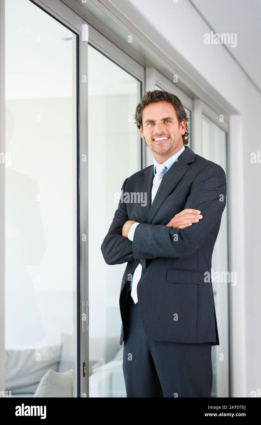 Homme d'affaires debout près de la porte en verre. Homme d'affaires intelligent se tenant près d'une fenêtre en verre avec les mains repliées. Banque D'Images