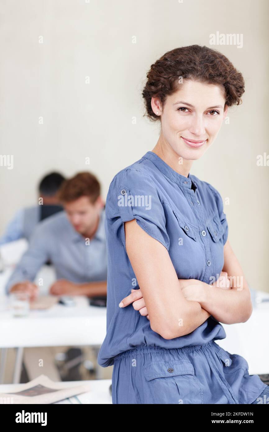 Nous prenons vos BESOINS INFORMATIQUES au sérieux. Portrait d'une employée de bureau confiante assise sur son bureau avec des collègues assis derrière elle. Banque D'Images
