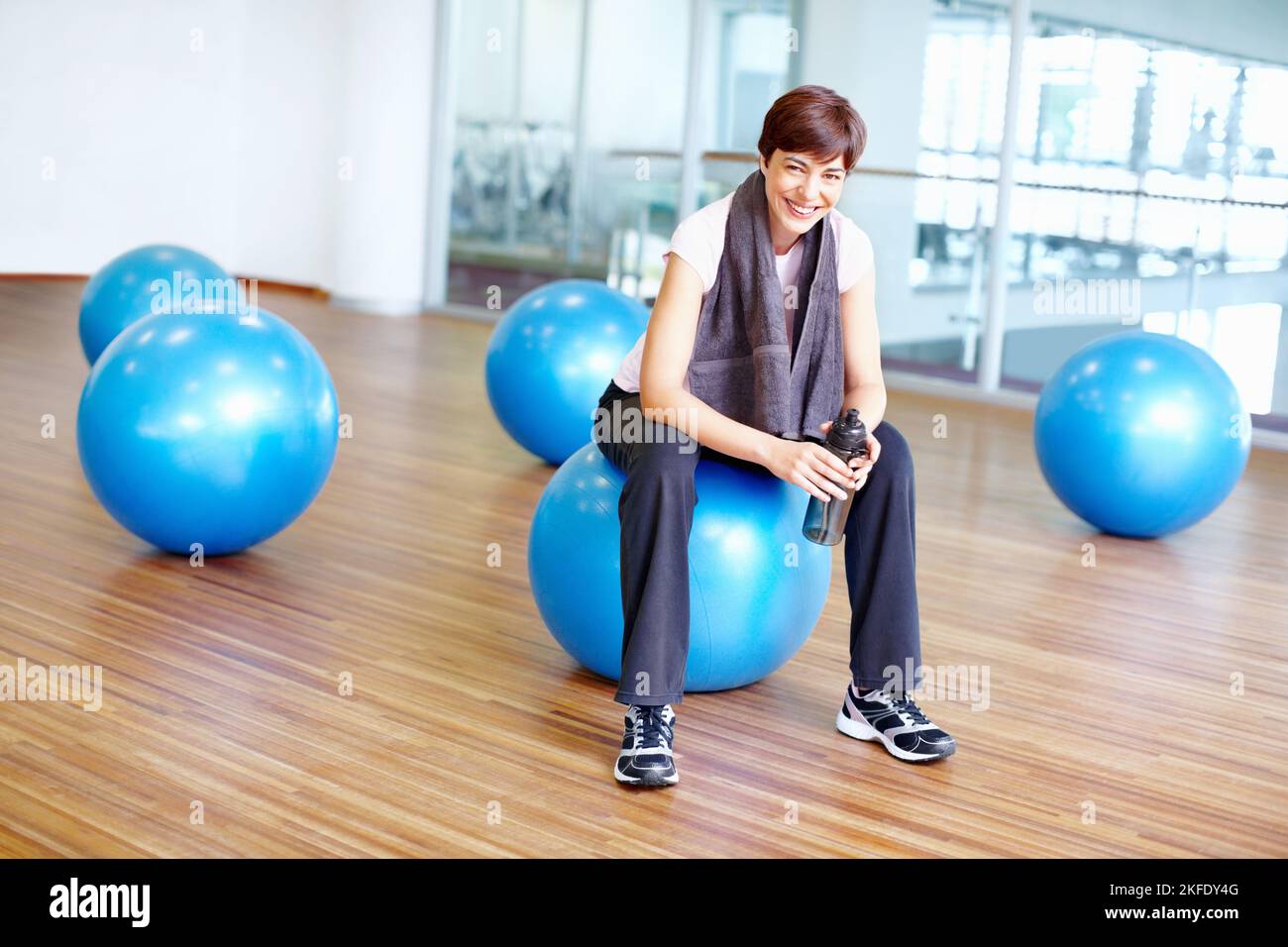 Femme assise sur le ballon pilates et souriant. Portrait de la femme souriante en forme assise sur le ballon pilates pendant sa session d'entraînement. Banque D'Images